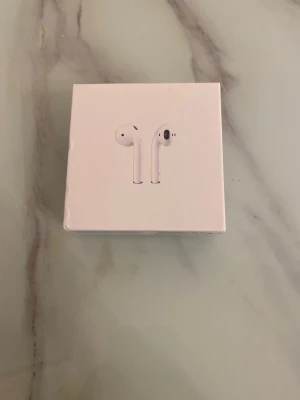 Apple AirPods trådlösa hörlurar - Säljer ett par vita Apple AirPods med laddningsetui. De är trådlösa och har en stilren, minimalistisk design i plast. Perfekta för musik, poddar och samtal. Kommer i originalförpackning.