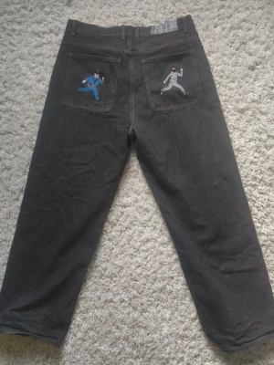 Poser jeans cops and robbers - Unika svarta jeans med raka ben och broderade figurer på bakfickorna – en i blå kostym och en i randig dräkt. Jeansen har klassisk femficksdesign och bälteshällor. Perfekta för dig som vill sticka ut med coola detaljer.