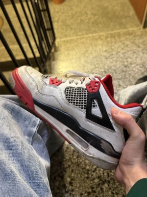 Air Jordan 4 Retro Fire Red sneakers - Snygga Air Jordan 4 Retro Fire Red sneakers med vit ovandel i läder, svarta och röda detaljer samt meshpaneler på sidorna. Klassisk siluett med synlig Air-enhet i sulan och röda accenter på snörningen. Perfekta för dig som gillar streetwear och ikoniska sneakers.