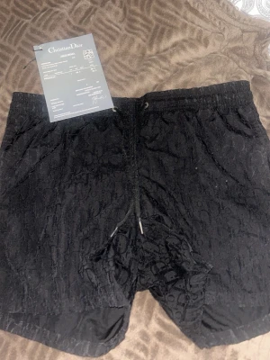Badbyxor från Christian Dior - Snygga svarta badbyxor från Christian Dior med diskret mönster i tyget och dragsko i midjan. Lyxig känsla och exklusiv design, perfekta för dig som gillar premiumunderkläder. Materialet känns mjukt och bekvämt mot huden.