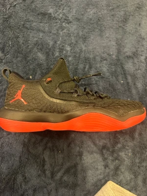 Svarta Air Jordan sneakers med röd sula - Snygga svarta Air Jordan sneakers med röd sula och röd Jumpman-logga på sidan. Ovandelen är i textil med mönstrad struktur och svarta skosnören. Skorna har en sportig siluett och detaljer i rött på plösen. Perfekta för dig som gillar streetwear och basketstil.