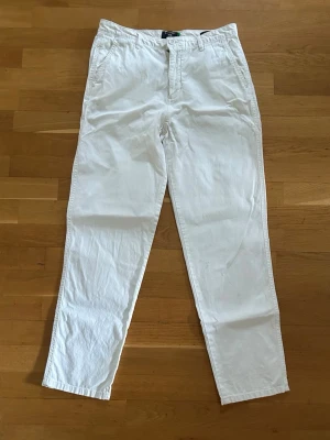 Vita chinos - Snygga vita chinos med rak passform och klassisk design. Byxorna har fickor fram och bak samt stängs med knapp och dragkedja. Perfekta för en clean och stilren look.