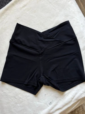Svarta bikershorts med V-formad midja - Säljer ett par svarta bikershorts med snygg V-formad hög midja. Tillverkade i stretchigt och mjukt material som passar perfekt för träning eller chill. Shortsens design ger en smickrande siluett och sitter bekvämt på kroppen.