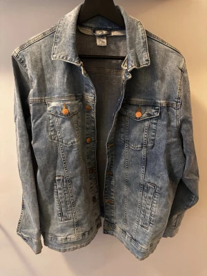 Klassisk ljusblå jeansjacka - Snygg ljusblå jeansjacka med klassisk passform och krage. Jackan har två bröstfickor med knappar och två sidofickor. Stängs med kopparfärgade knappar framtill. Perfekt för en avslappnad streetstyle-look.