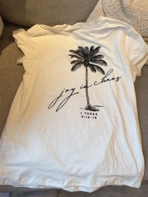 Ny i förpackning! Vit t-shirt med palmtryck och text - Snygg vit t-shirt med svart palmtryck och text. T-shirten har en avslappnad passform och är tillverkad i mjukt material, perfekt för en chill och stilren look.