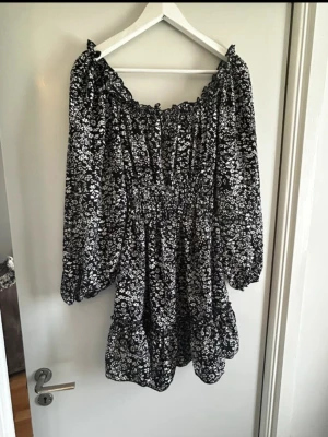 Mini klänning - Mini klänning med smock runt midjan. Går att ha helt of shoulder eller med rundad urringning på axlarna. Mest svart och vit med få röda blommor.