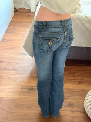 Vintage Bootcut jeans  - Säljer ett par blå bootcut jeans med snygga fickdetaljer bak och fram. Jeansen har låg midja, dekorativa sömmar och knappstängning. Jättefina men inte min stil💕💕