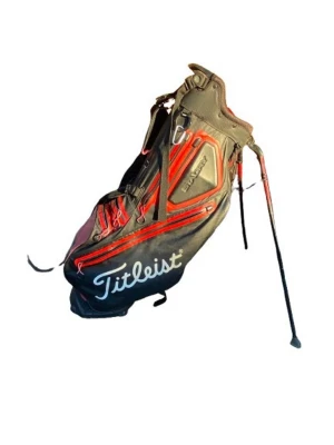 Svart och röd golfbag från Titleist - Golfbag från Titleist i svart och rött med flera fack och tydlig logga på sidan. Utrustad med benstativ för enkel placering på marken och praktiska bärremmar. Invändigt finns röda avdelare för klubbor. Perfekt för golfbanan. 