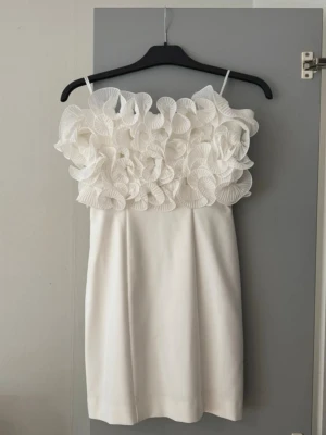  Ny slutsåld Vit offshoulder kortklänning med volangdetaljer - Superfin vit kortklänning med  stora volangdetaljer upptill. Klänningen har en rak passform och är perfekt för dig som vill sticka ut med en unik och trendig look. Materialet känns mjukt och har en lyxig känsla.