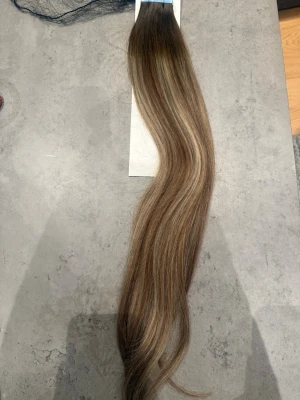 Långt löshår med balayage-effekt - Snyggt löshår med tejpfästen i en naturlig balayage med mörkbrun botten och ljusare blonda längder. Håret är rakt och har en mjuk glans. Perfekt för dig som vill ha extra längd och volym. Material: äkta hår. Säljer då jag köpte för mycket, 