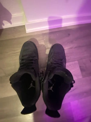 Svarta Air Jordan 4 Retro sneakers - Säljer ett par helsvarta Air Jordan 4 Retro sneakers med klassisk Jumpman-logga på plösen och sulan. Skorna har meshpaneler på sidorna, plastdetaljer och en robust sula. Perfekta för dig som gillar streetwear och vill sticka ut med en ikonisk siluett. UTAN ORGINALBOX OCH KVITTO