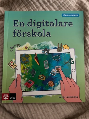 En digitalare förskola - Boken 'En digitalare förskola' av Katrin Jäverbring handlar om digital kompetens i förskolan. Omslaget är grönt med illustrationer av en surfplatta och digitala ikoner. Perfekt för dig som vill utforska digitala verktyg och metoder i pedagogisk verksamhet.