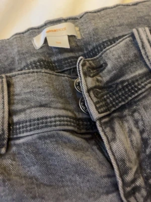Grå tvättade jeans från Gina Tricot - Snygga grå jeans från Gina Tricot med tvättad look och dubbla knappar i midjan. Jeansen har klassisk femficksmodell och raka ben. Perfekta för en trendig och avslappnad stil.