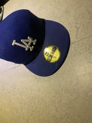 Blå New Era 59FIFTY LA keps - Snygg blå keps från New Era 59FIFTY med LA-logga broderad i silver framtill. Klassisk flat brim och sticker kvar på skärmen. Perfekt för dig som gillar streetwear och sportig stil.