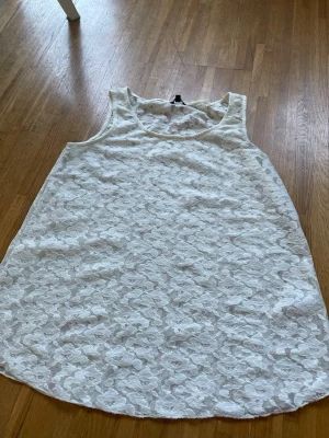 Vit spetsärmlös linne - Snygg vit ärmlös linnetopp med spetsdetaljer och blommigt mönster. Perfekt för en fräsch och somrig look. Rund halsringning och lätt, luftig känsla. Passar till både jeans och kjol. Lite see-trough. 