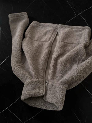 Beige teddyjacka med dragkedja - Mysig teddyjacka i beige med dragkedja framtill. Jackan har en fluffig utsida och mjuk insida, perfekt för kyliga dagar. Enkel och stilren design utan synligt märke. Passar dig som gillar en avslappnad och trendig look.