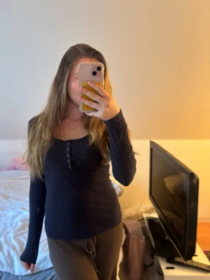 Mörkblå ribbad långärmad topp - Mörkblå långärmad topp med ribbad struktur och knappar framtill. Snygg och enkel modell med rund halsringning, perfekt att matcha med jeans eller kjol.