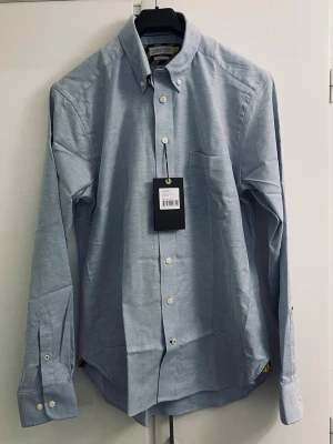 J. Harvest & Frost Yellow Bow Skjorta slim fit - Klassisk ljusblå skjorta från Brooks Brothers med button-down krage och bröstficka. Skjortan har vita knappar och långa ärmar. Perfekt för en clean och stilren look.