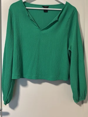 Grön långärmad blus från LINDEX - Grön blus från LINDEX med lång ärm och v-ringad krage. Blusen har en lätt rynkad struktur i tyget och avslappnad passform.