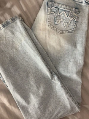 Ljusblå jeans från Wrangler - Snygga ljusblå jeans från Gina med klassisk femficksdesign och broderad W-logga på bakfickan. Jeansen har en bootcut passform och är tillverkade i mjuk denim med lätt tvättad look. Perfekta för en avslappnad och trendig stil.