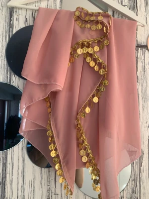 Rosa sjal med guldmynt - Snygg rosa sjal i tunn chiffong med dekorativa guldfärgade mynt längs kanterna. Perfekt accessoar för att ge din outfit en unik och festlig touch. Lätt och luftig, passar bra att drapera över axlarna.
