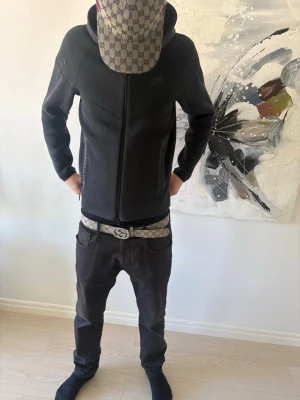 Svart Nike hoodie med dragkedja - Säljer en svart hoodie från Nike med dragkedja framtill och huva med dragsko. Hoodien har en stilren design med diskret Nike-logga på bröstet. Perfekt för dig som gillar en clean och sportig look. Materialet känns mjukt och bekvämt.