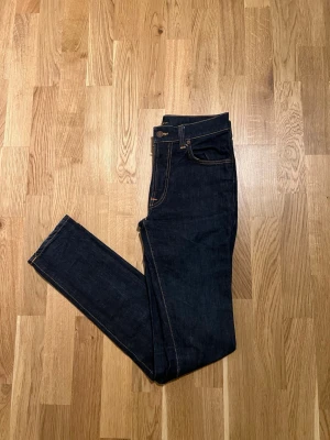 Mörkblå Nudie Jeans - W30/L34 - Klassiska mörkblå Jeans för män, Storlek Waist 30 / Lenght 34. Mycket bra skick inga skador/slitage. Hör av dig vid intresse/frågor. PRIS KAN DISKUTERAS!