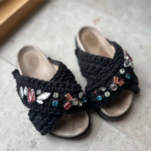 Inuikii Woven Sandals Storlek 37 - Säljer ett par unika svarta stickade sandaler från Inuikii i storlek 37. De har en cool design med stora, färgglada pärlor i olika former och färger som ger en glittrig och festlig look. Perfekta för sommaren och att sticka ut på festen! Nypris är cirka 3000kr. Saknas en liten sten men det är knappt ngåot som syns, se bild 4. Stora i storleken och passar även 38. köpte de precis innan sommaren men har använts mycket men de är fortf i bra skick!