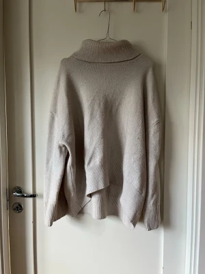 Beige stickad polotröja - Mysig beige stickad polotröja med oversized passform och breda ribbade muddar vid ärmslut och nederkant. Perfekt för lager-på-lager och chill höststil. Hög krage som ger extra värme och stilpoäng.