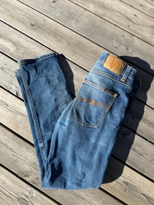 Nudie Jeans Lean Dean - Ett par klassiska blå jeans från Nudie Jeans med slim passform och fem fickor. Jeansen har tydliga orange sömmar, läderpatch med logga bak och är gjorda i denim. Perfekta för dig som gillar en enkel och stilren look. Storleken är W30 L30. Modellen är Lean Dean, riktigt bra pris!