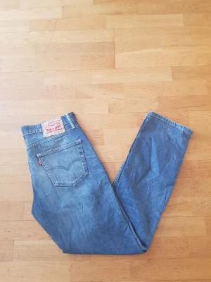 Levi's 511 blå jeans - Säljer ett par klassiska blå Levi's 511 jeans med rak passform och fem fickor. Jeansen har den ikoniska röda Levi's-lappen på bakfickan och patch i midjan. Perfekta för en avslappnad och stilren look.