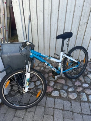 Blå och vit mountainbike Scott  - FRAKT TILLKOMMER/ UPPHÄMTAS I BÅLSTA. Säljer en blå och vit mountainbike från Scott med svart sadel och handtag. Cykeln har grova däck, framgaffel med fjädring och reflexer på hjulen. Passar perfekt för dig som vill ha en cool cykel till vardagsäventyr.