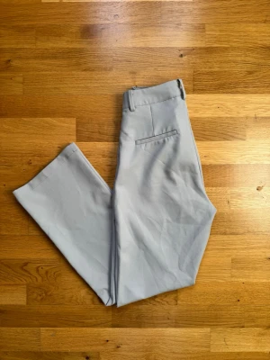 Ljusgrå kostymbyxor med utsvängda ben - Snygga ljusgrå kostymbyxor från Gina Tricot med utsvängda ben och klassisk passform. Byxorna har hällor för skärp, snedställda fickor fram och en dekorativ bakficka. Perfekta för en stilren look.
