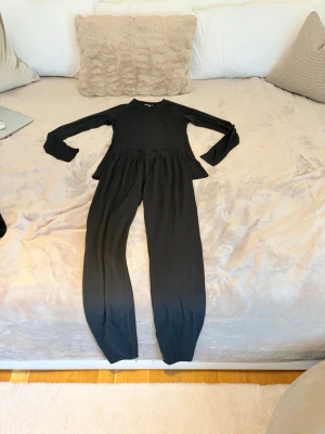 Svart set med långärmad topp och byxa - Säljer ett svart set med långärmad topp och matchande byxa. Setet har enkel, stilren design och är gjort i ett mjukt, stretchigt material som känns skönt mot huden. Perfekt för dig som gillar minimalistisk stil och vill ha något bekvämt att bära hemma.