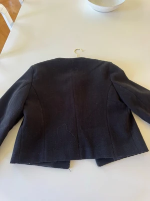 Svart cardiganjacka från Zara - Stilren svart cardiganjacka från Zara med rund halsringning och fyra fickor framtill. Jackan har guldknappar och är tillverkad i ett mjukt tyg med rak passform.