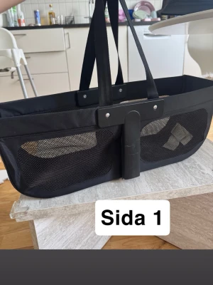 Svart sidokorg från Bugaboo Donkey - Säljer en svart sidokorg från Bugaboo Donkey. Finns tecken på användning såsom skrapmärken/repor. Fullt funktionsduglig! Korgen har meshpaneler på sidorna och dubbla handtag för enkel bärning. Tillverkad i slitstarkt tyg och plastdetaljer. Passar till barnvagn eller som praktisk shoppingväska. 