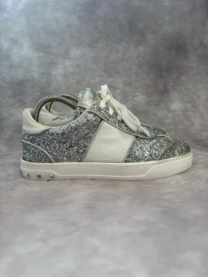 Valentino Flycrew Glitter Skor - Stl 36,5 - Fina Valentino skor i vitt och silver, perfekt till våren och sommaren! 🌷🏖️ | Mycket bra skick: 8,5/10, lossnat lite vid höger häl (se bild) syns inte väll vid användning och går att lösa oss skomakare 🙌, saknar 1 nit | Storlek: 36,5  | Ingår: Endast Skorna 🙌 | Nypris: Ca 5500kr | Självklart äkta. Hör av dig vid frågor // Galgen 🫡