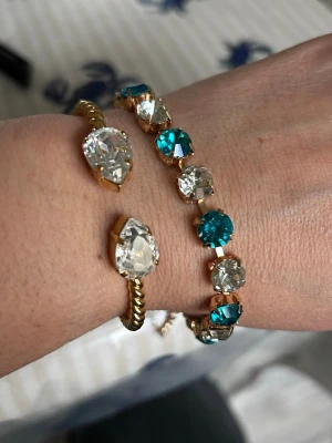 Armband med blå och klara kristaller - Rostfritt snyggt armband med stora runda kristaller i turkosblått och klart, infattade i guldfärgad metall. Armbandet har ett justerbart kedjelås och ger en riktigt glittrig look. Perfekt för dig som gillar att sticka ut med färg och bling.liknar Caroline Svedbom armband 