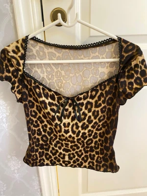 Leopardmönstrad topp med rosett - Trendig topp med leopardmönster, v-ringning och liten svart rosett framtill. Korta puffärmar och dekorativ spetskant längs halsringningen. 
