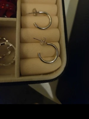Två par silvriga hoops örhängen - Säljer två par stilrena hoops i silverfärgad metall. Ena paret är klassiska runda hoops med stift, det andra paret är något tjockare och har en modern, kantig design. Perfekta för att lyfta din look med en enkel touch av metall.