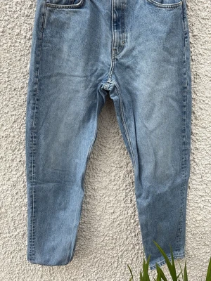 Ljusblå mom jeans från LASH - Säljer ett par ljusblå mom jeans från weekday med klassisk femficksdesign och hög midja. Jeansen har raka ben och är tillverkade i 100% bomull för en skön vintagekänsla. Perfekta för en avslappnad och trendig look.