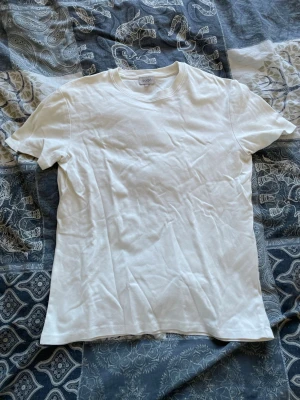 Vit t-shirt från Sandö i bomull - Klassisk vit t-shirt från Sandö i mjuk bomull. Enkel design med rund hals och korta ärmar, perfekt till jeans eller shorts. Passar dig som gillar en stilren och basic look.