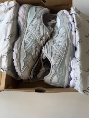 Asics GEL-NYC grå sneakers - Snygga Asics GEL-NYC sneakers i ljusgrå och silver med vita detaljer. Ovandelen är i mesh och syntetmaterial för bra andningsförmåga och komfort. Sulan är vit med inslag av grått och har GEL-dämpning för extra skön känsla. Perfekta för en sportig och trendig look. De passar ej mig därför jag säljer. Allt tillkommer. ( box lite sönder ) PRIS KAN DISKUTERAS