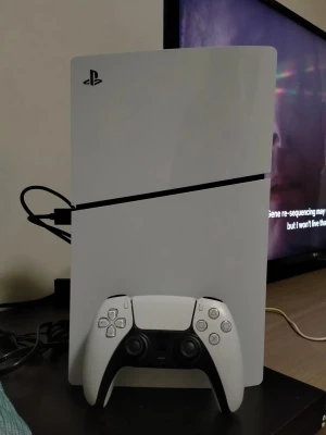 Vit PlayStation 4 med handkontroll - Snygg vit PlayStation 4 med tillhörande vit och svart DualShock 4-handkontroll. Konsolen har en stilren, rektangulär design med svarta detaljer och PlayStation-loggan i hörnet. Perfekt för gaming och streaming.