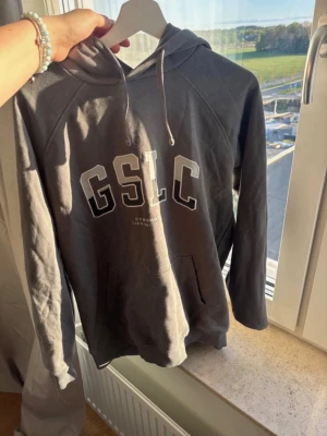 Mörkgrå hoodie GSLC - Snygg mörkgrå hoodie från gymshark med stor vit logga på bröstet och klassisk känguruficka. Hoodien har huva med dragsko och långa ärmar, perfekt för en chill och sportig stil.