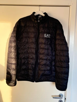 EA7 emporio Armani jacka  - Säljer en äkta mörkblå kviltad lättviktsjacka från EA7 Armani. Perfekt inför våren då den är lätt och smidig. Originalpåse medföljer. Certilogo finns för äkthetskontroll. Storlek XXL, men då EA7 är små i storlek (Slim Fit) passar den mer som Large eller XL. Skick: Bra begagnat skick men har spår av användning i form av naturligt dunsläpp vid sömmarna på flera ställen, vilket är vanligt för modellen. Dragkedjan fungerar fint. Pris kan diskuteras, skambud undanbedes 