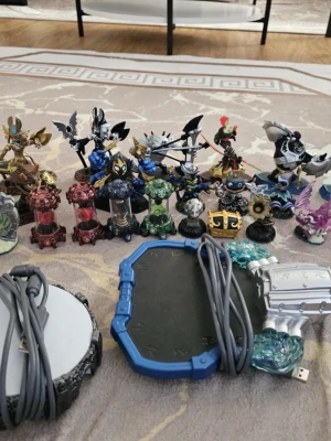 Skylanders spel och figurer - Samling med Skylanders-figurer i olika färger och former samt två portaler med USB-kablar. Figurerna är tillverkade i plast och föreställer olika karaktärer och element. Perfekt för dig som vill utöka din Skylanders-samling eller spela på konsol.
