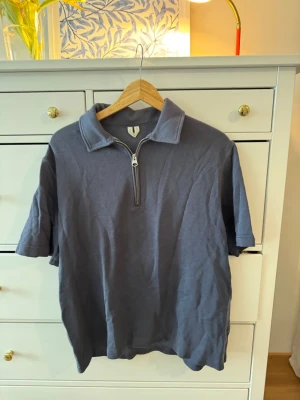 Blå polotopp med half zip - Snygg blå polotopp med kort ärm och dragkedja framtill. Toppen har en klassisk krage och är gjord i mjukt bomullsmaterial. Perfekt för en avslappnad och trendig look.