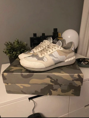 valentino rockrunners i grått och vitt  - Snygga sneakers från Valentino i beige, vitt och grått. Skorna har en låg siluett, mockadetaljer och meshpaneler för extra andningsförmåga. Klassisk snörning och gummisula ger en clean och modern look. Perfekta för dig som gillar stilrena och trendiga sneakers.  PRIS KAN DISKUTERAS