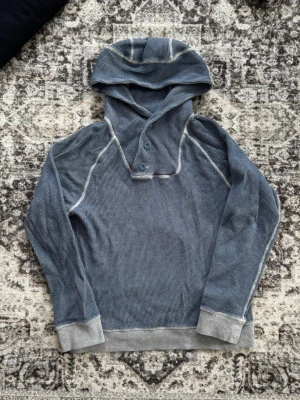 Vintage Blå hoodie med knappar och huva - Säljer en vintage blå hoodie i waffle-mönstrad bomull med kontrastsömmar och grå muddar. Hoodien har en snygg stor luva. Storlek S/M.